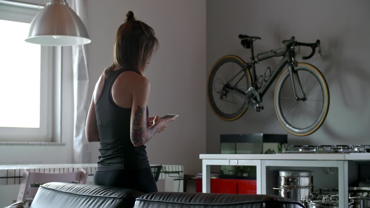 joven tatuada usando teléfono inteligente para el seguimiento durante el entrenamiento deportivo de fitness en el hogar.entrenamiento doméstico en la sala de estar. video en cámara lenta 4k