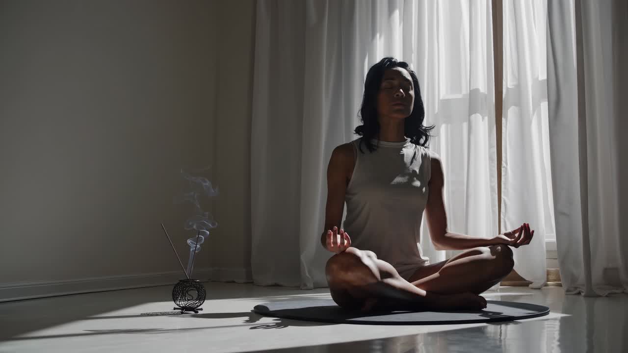 Una serena scena video di una persona che medita in una stanza illuminata dal sole. Girata da un angolo basso, cattura