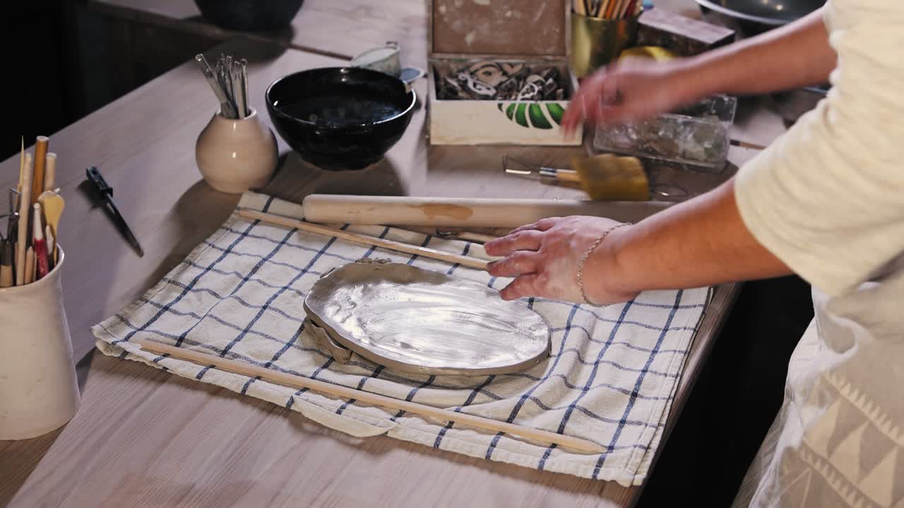 스튜디오 의 도자기 - 젊은 여자 가 스폰지 를 사용 하여 평평 한 점토 조각 의 표면 을 인다