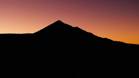 Panning-drone-aerial-shot-of-a-mountain-silhouette-with-colorful-background