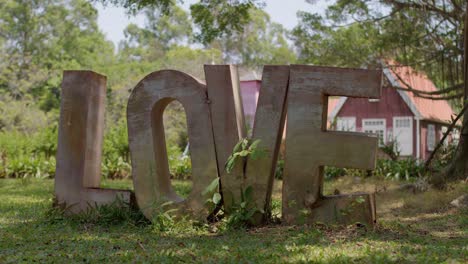 Metal-letters-forming-word-LOVE-standing-in-the-shadow-of-tree-near-German-style-house-in-background-on-a-bright-sunny-day