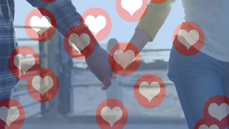 multiple red heart icons floating against mid section of couple holding hands and walking