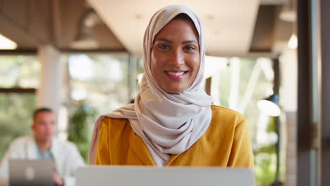 Portrait-Of-Mature-Businesswoman-Wearing-Headscarf-Working-On-Laptop-At-Desk-In-Office