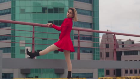 en un tejado en port of spain, trinidad, una joven hispana está elegantemente de pie en un vestido rojo, edificios altos enmarcan la escena