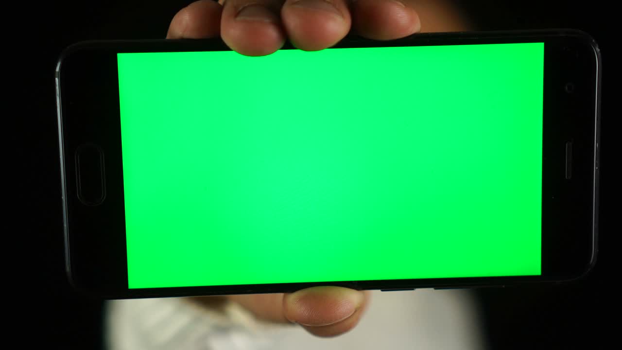 크로마 키와 녹색 화면을 가진 스마트 폰을 보여주는 인식할 수 없는 남자