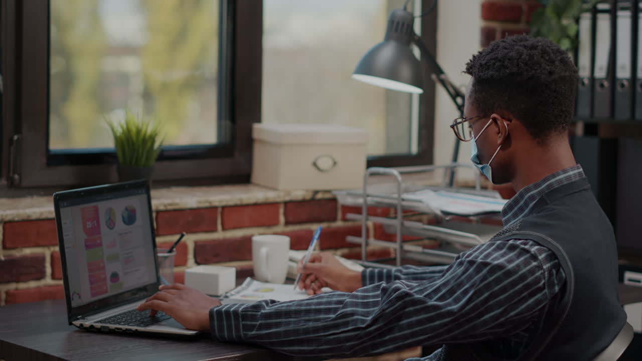 Financial consultant with face mask planning sales report on laptop