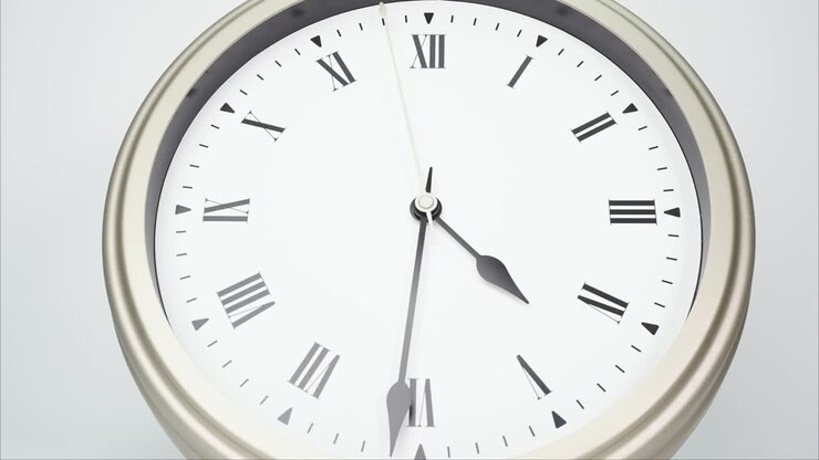 Time lapse silver wall clock tells the time at 5 o'clock.