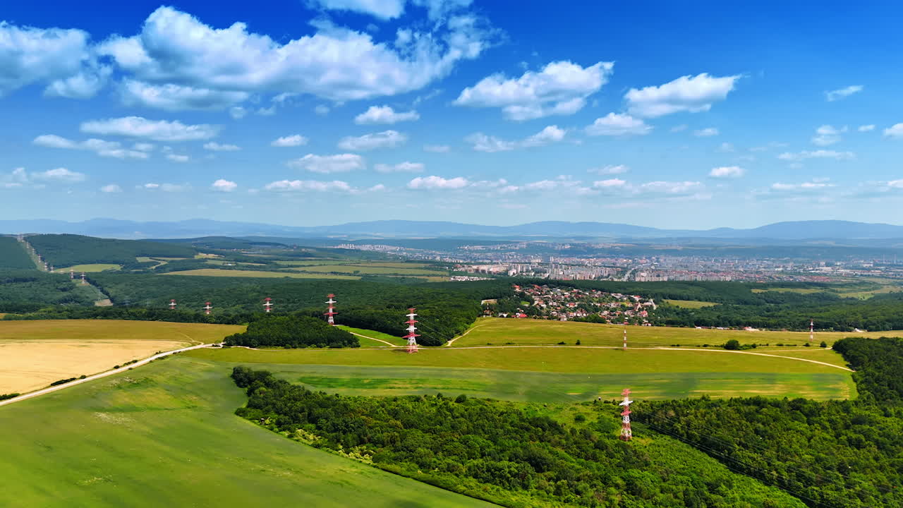 Vast fields and city view. Lush green fields stretch out towards a distant city under a bright blue sky, revealing communication towers