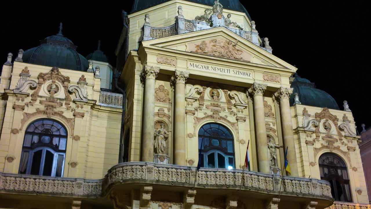 Nighttime view of the National Theatre of Pécs, beautifully illuminated, highlighting its ornate facade and historic architecture