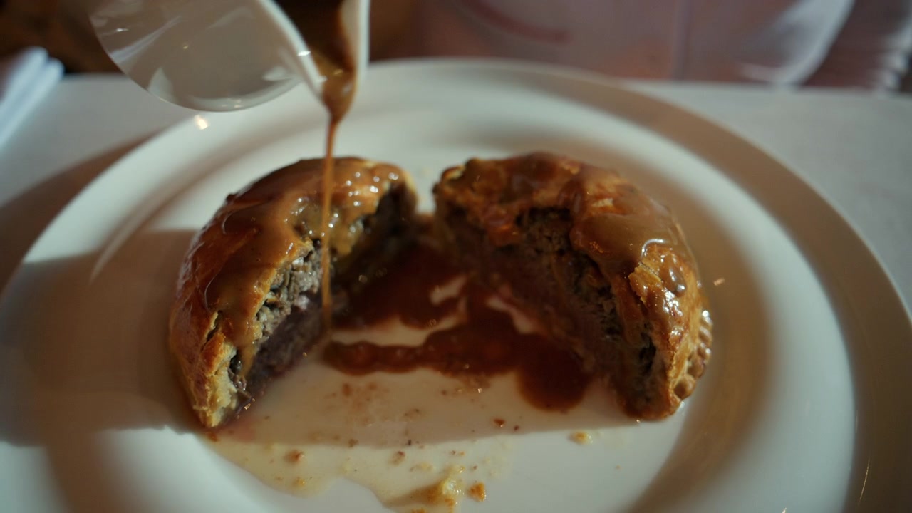 Sauce riche versée sur un Bœuf Wellington tranché dans un restaurant gastronomique.