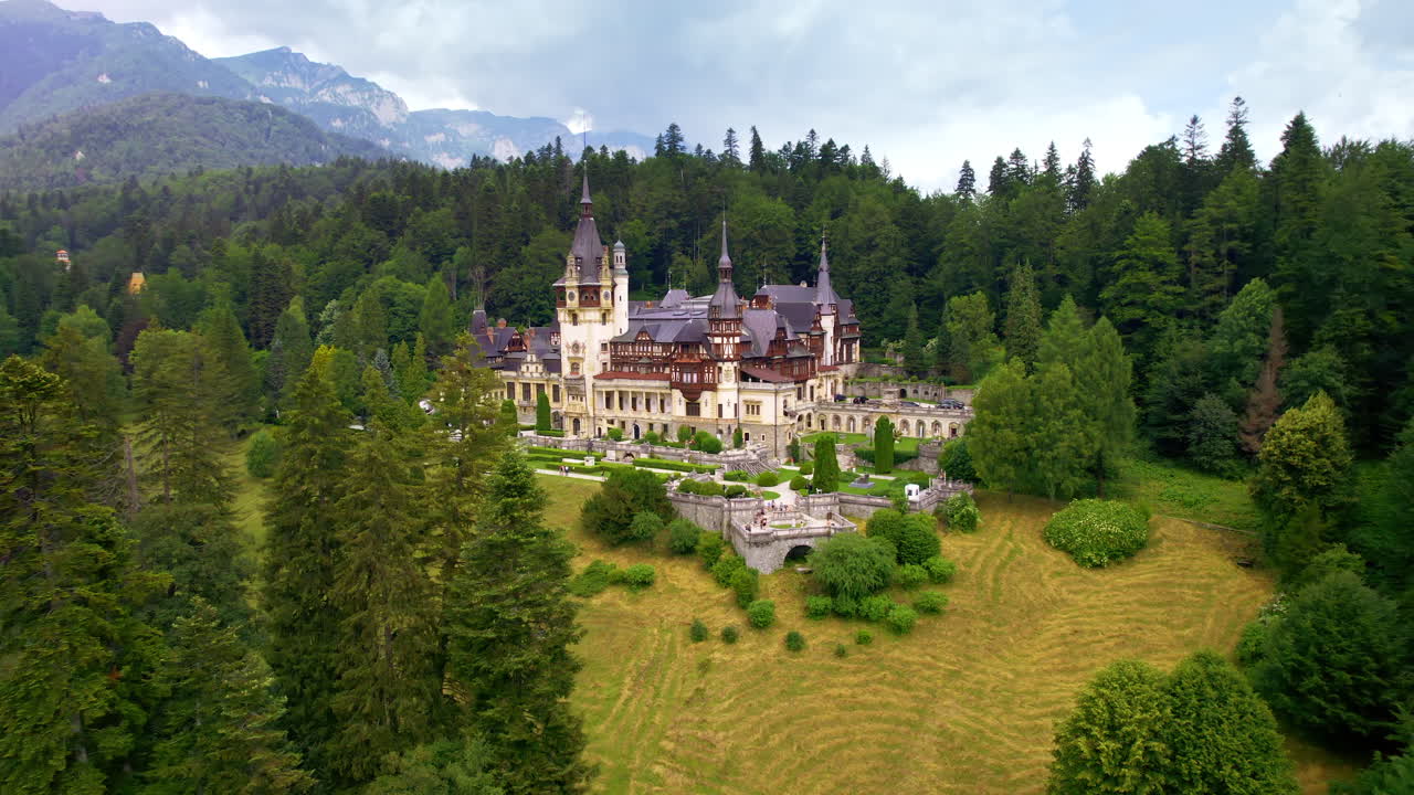 Luftdrone-utsikt over Peleș slott i Romania. Slott med hager og turister i Karpatene, frodig skog rundt.