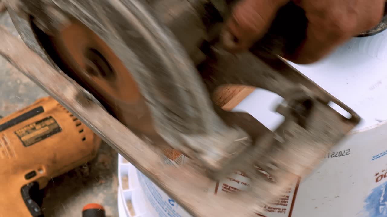 Crafty carpenter cuts with an industrial circular saw machine in half a small thin piece of wood to elaborate forniture in his outdoor traditional workshop small business