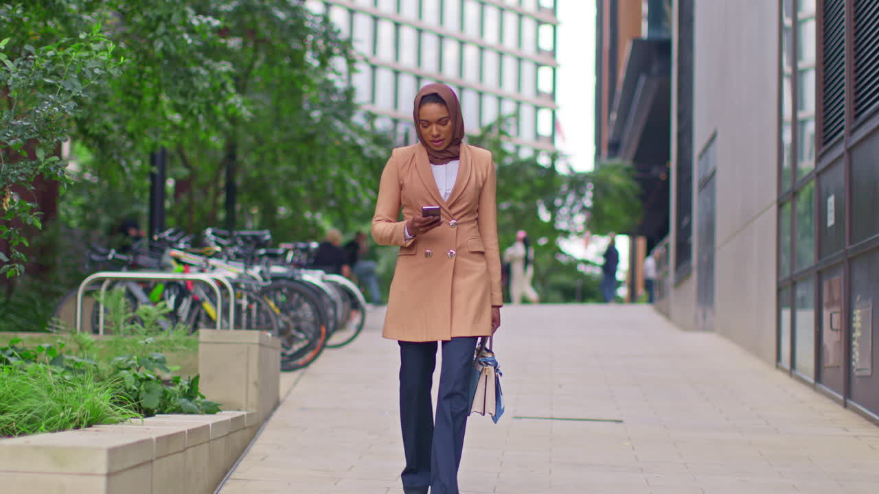 Muslim Businesswoman Wearing Hijab Going To Work Standing Outside Modern Office Looking At Mobile Phone 5