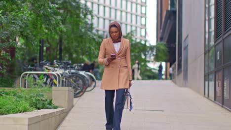 muslim businesswoman wearing hijab going to work standing outside modern office looking at mobile phone 5