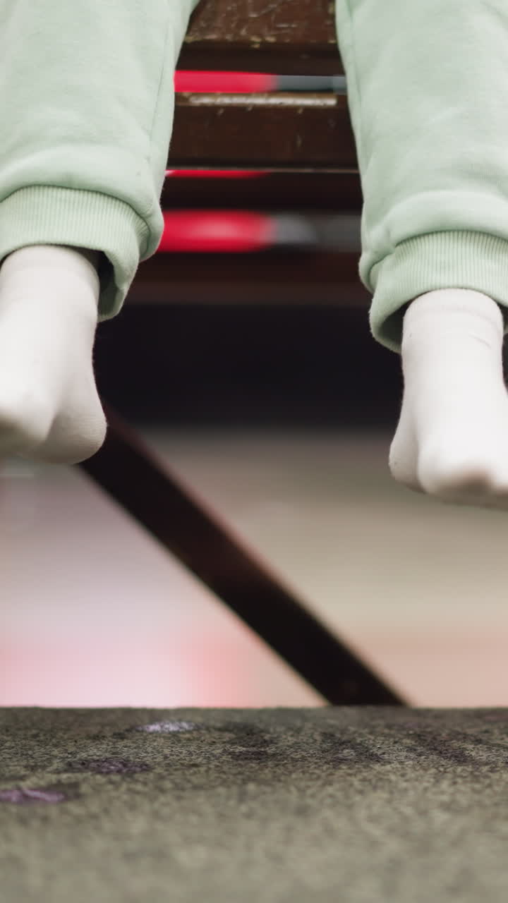 una vista cercana de una persona sentada en un banco, con calcetines blancos y pantalones verdes, con patines de hielo rosados colocados al lado de la persona, la persona cuelga sus piernas jugosamente