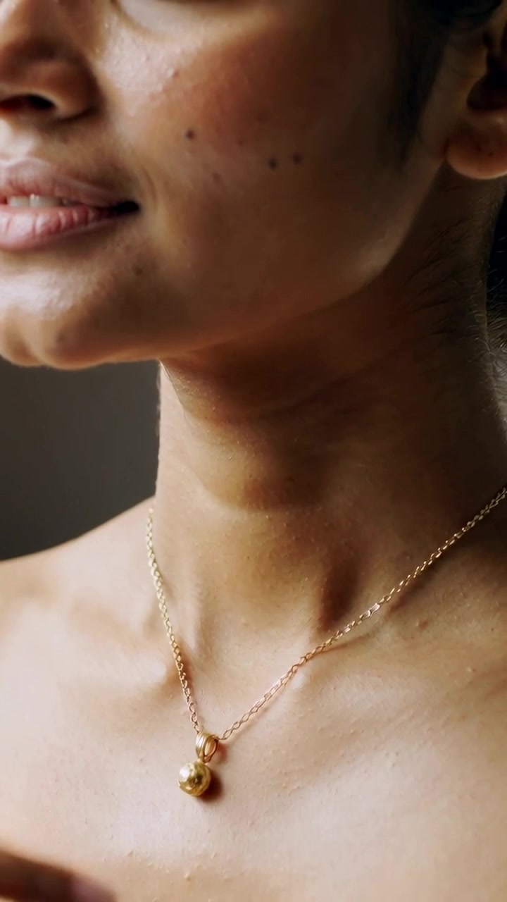 Video verticale: Una donna che afferra e centra un ciondolo di catena d'oro sul collo, in una stanza con le spalle scoperte.