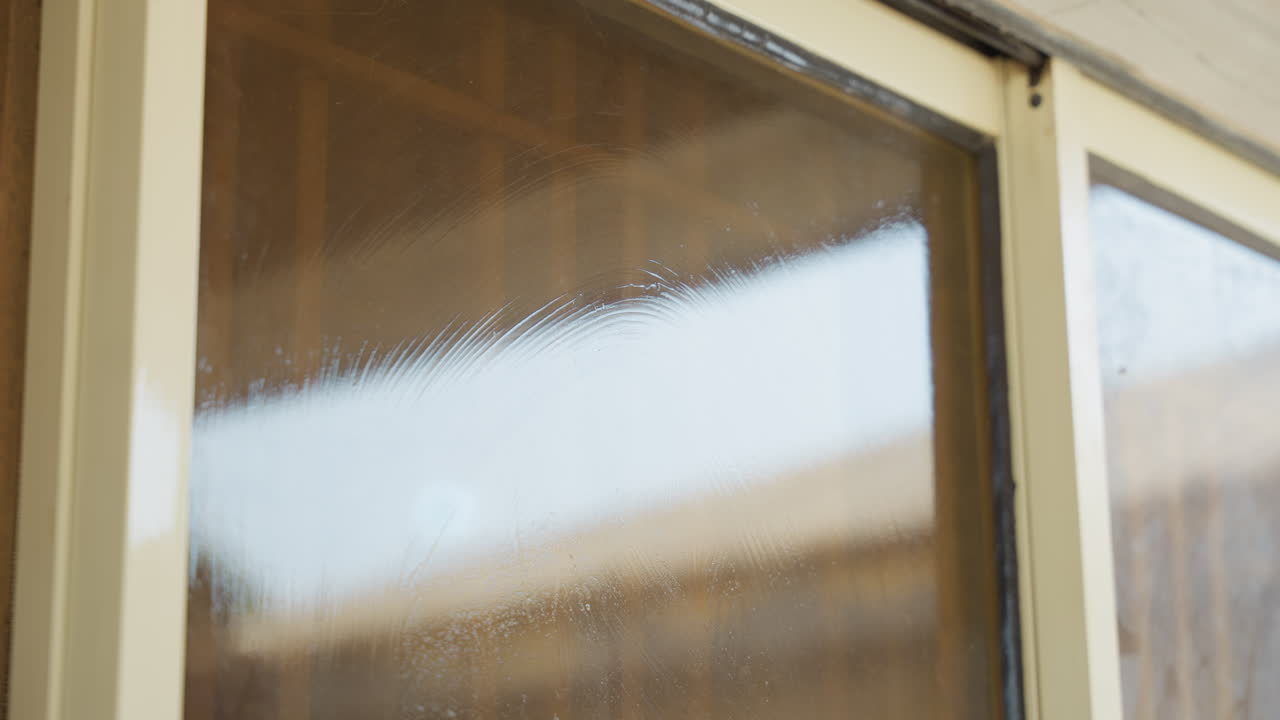 Closeup hand cleaning window frame with cloth and gentle pressure, concentrated focus on edge and corner, precise motions removing suds and streaks, calm domestic maintenance at house