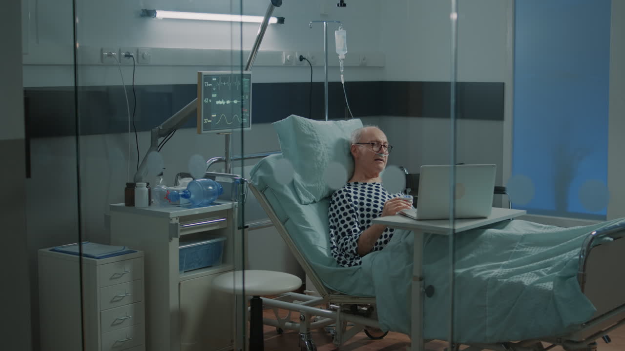 Elder sick patient using laptop in hospital ward bed