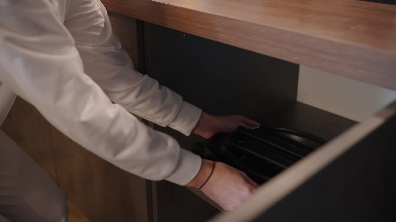 Woman putting pots and pans in a kitchen drawer.