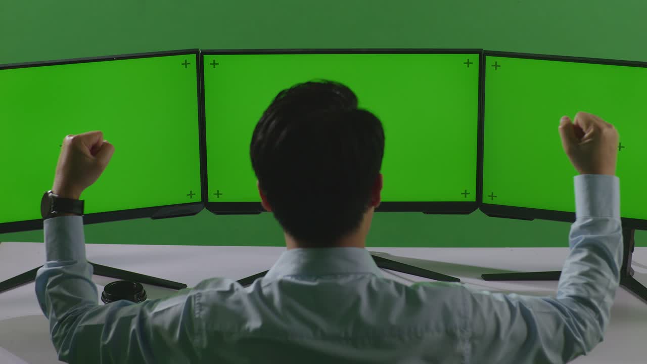 Back View Of Happy Asian Man Celebrating While Working With Mock Up Multiple Computer Monitor In Green Screen Studio