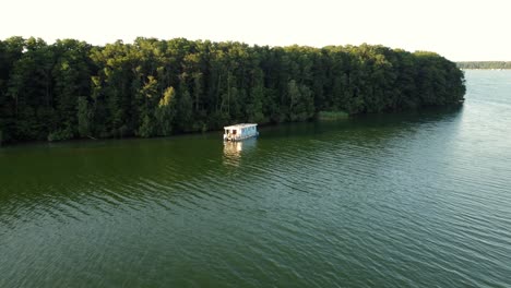 Pequeña-Casa-Flotante-Flotando-En-Un-Lago-Junto-A-Un-Bosque-Y-Varias-Otras-Embarcaciones-A-Motor-En-Brandeburgo,-Alemania