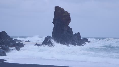 dramatic waves crashing against unique rock formations on a black sand beach in iceland under overcast skies