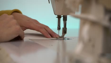 woman's hands guiding white fabric in sewing machine, slow motion close up