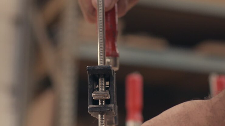 Craftsman screws down vise clamp onto wood in shop, close up slow motion