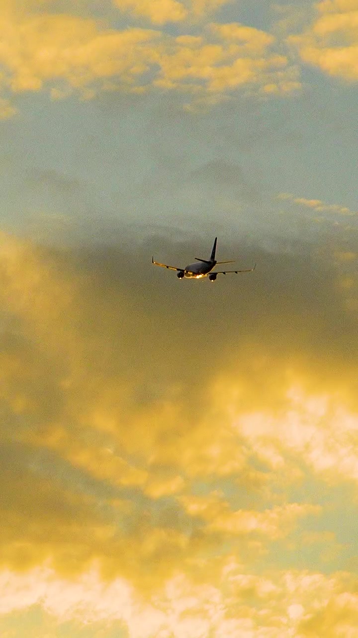 Et filmisk skud af et passagerfly, der daler ned gennem levende orange solnedgangsskyer. Ideel til temaer om rejser, luftfart og global forbindelse