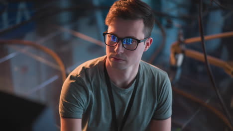 person working in tv studio, adjusting equipment and monitoring screen. close-up of focused face with glasses, studio lights and video equipment visible in background