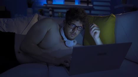 Young-man-using-laptop-at-night,-texting,-doing-research.