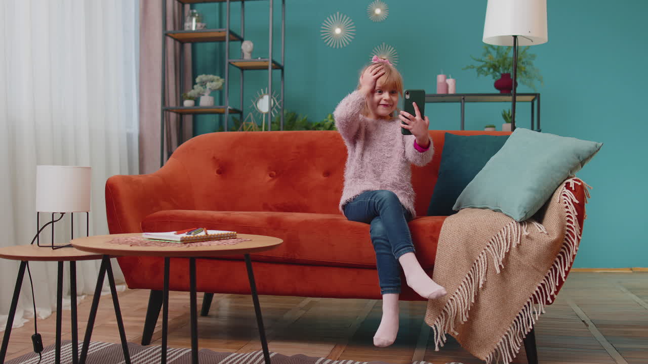 흥분한 우승자 소녀는 휴대전화를 사용하고 와우라고 말하며 놀란 손을 들고 혼자 집에 있습니다.