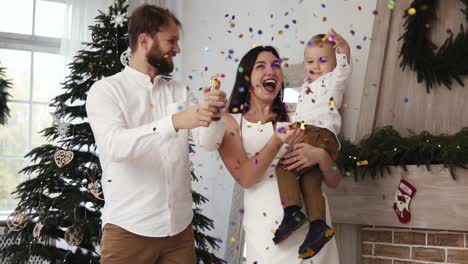 año nuevo, el joven padre está haciendo estallar fuegos artificiales, destellos de fuegos artificiales y confeti volando en el aire. familia alegre con lindo