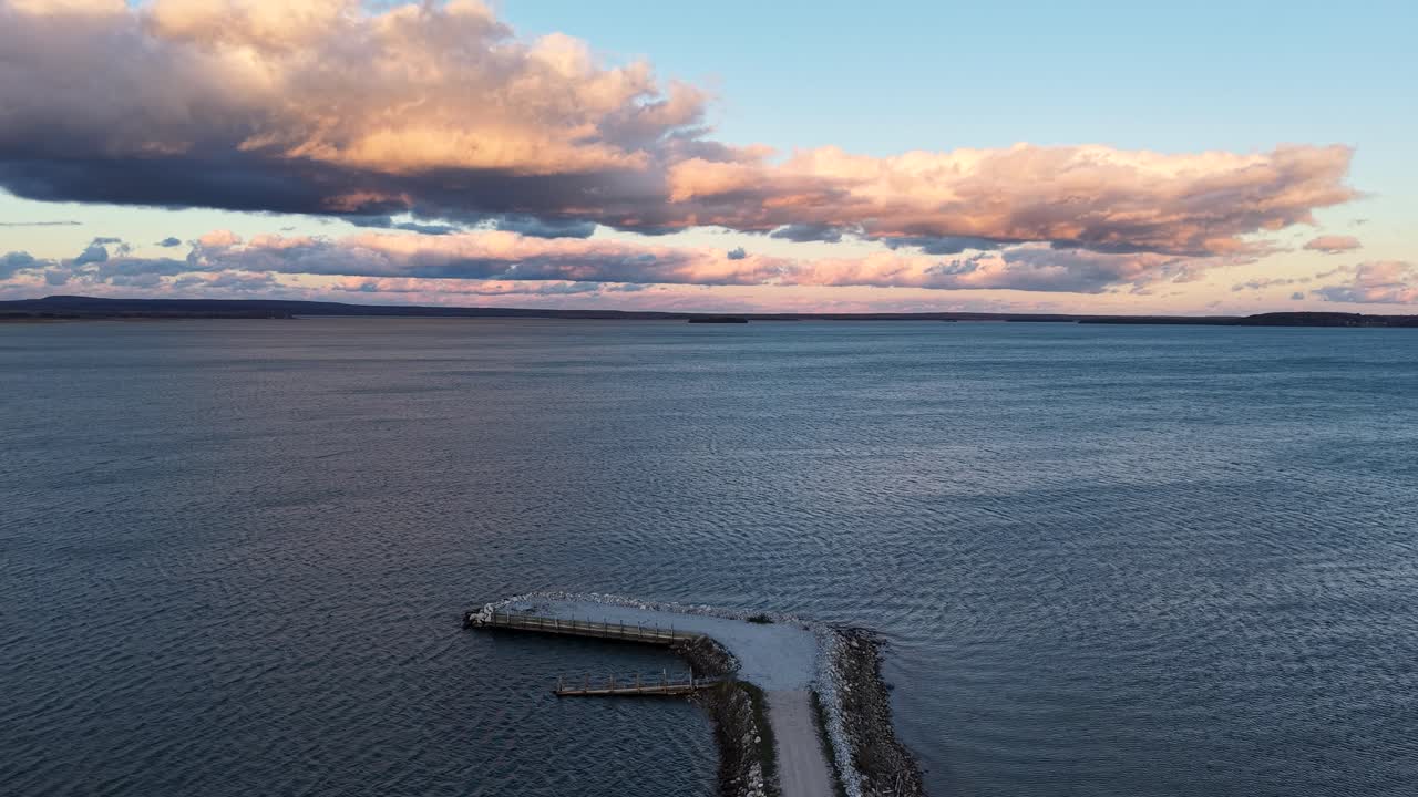 Aerial drone video of a breakwater extending into Lake Superior beneath a glowing sunset sky with dramatic clouds
