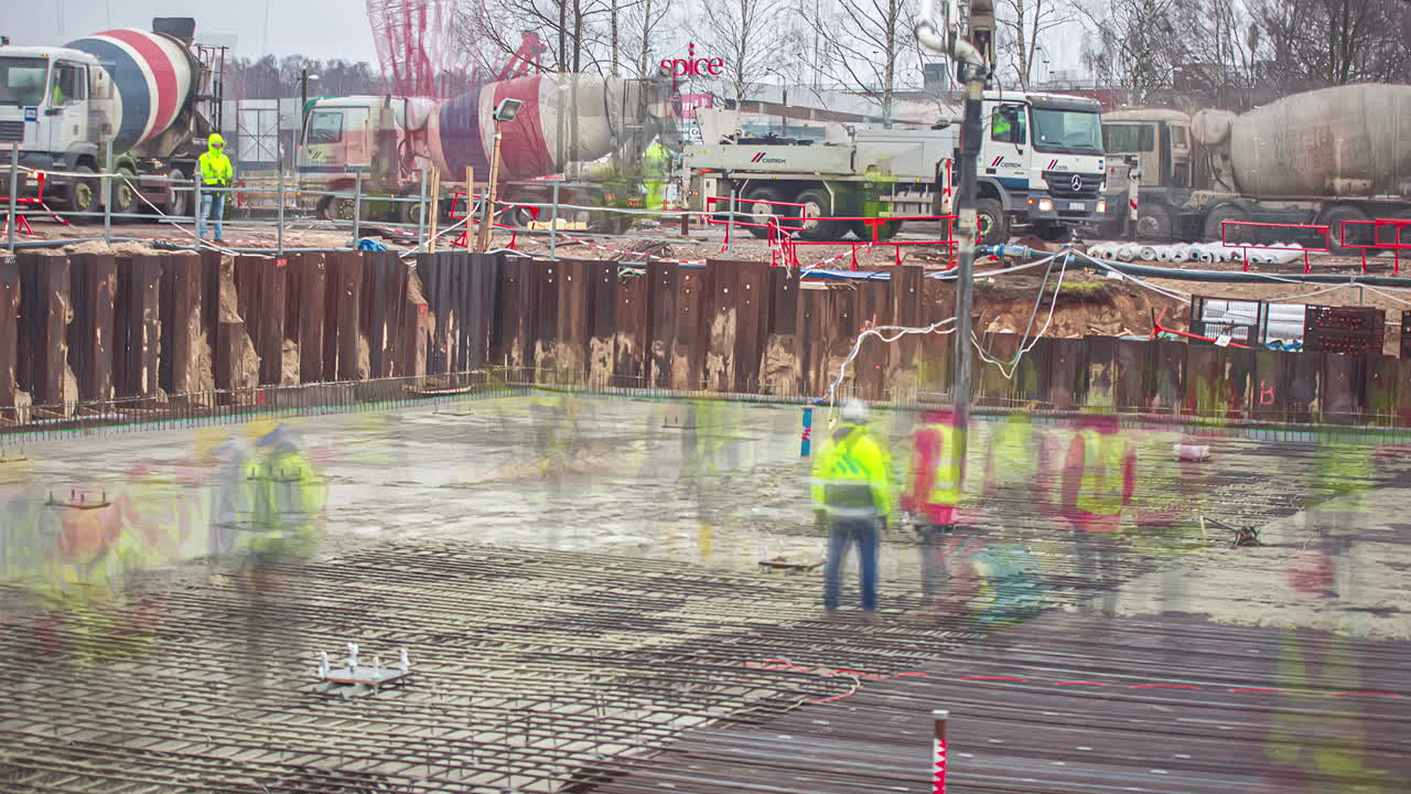 View of a busy building construction site in timelapse during autumn. Workers working at a construction site in Riga, Latvia (2018)with many concrete mixer trucks lined up delievering cement