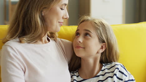 Close-Up-Of-The-Pretty-Mother-Hugging-And-Stroking-Her-Cute-Nice-Daughter-While-Sitting-On-The-Sofa-At-Home