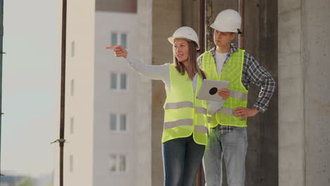 trabajador de la construcción hombre y arquitecto mujer en un casco discutir el plan de construcción de la casa hablar el uno al otro sobre el diseño sosteniendo una tableta mirar los dibujos fondo de los rayos del sol.