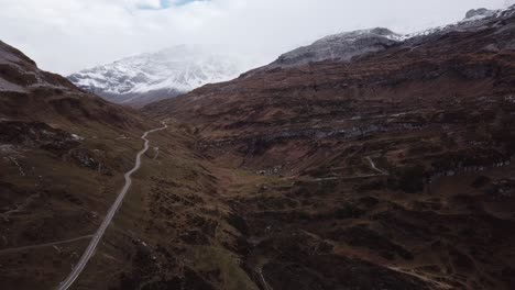 Aerial-shot-of-a-rocky-mountain-landscape-criss-crossed-by-winding-roads-and-snowy-hills-in-the-background