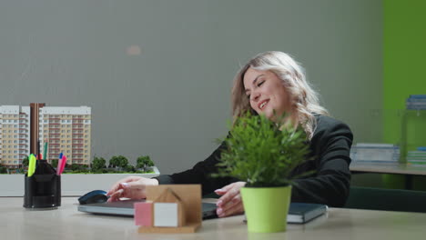 business expert joyfully speaks on phone with client, preparing to sit down and open laptop to begin work, surrounded by office decor and architectural project model