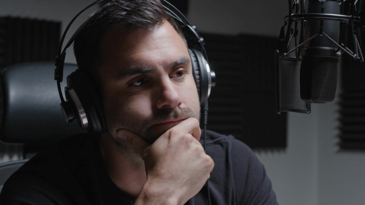 Inspelningssignal startar, man i mörk skjorta och headset lyssnar, övervakar upphängd mikrofon i studio.