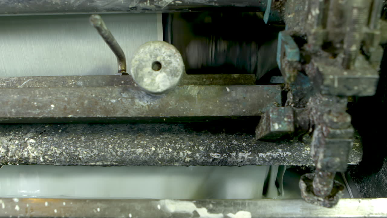 Closeup detail shot of an old and well-worn machine printing green wallpaper, using a tray of liquid light green paint.