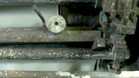 closeup detail shot of an old and well-worn machine printing green wallpaper, using a tray of liquid light green paint.