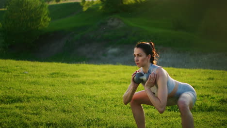 una mujer en cuclillas con pesas en el parque al atardecer realizando estocadas hacia el lado. motivación y entrenamiento deportivo. una mujer soltera hace ejercicios al atardecer en el verano