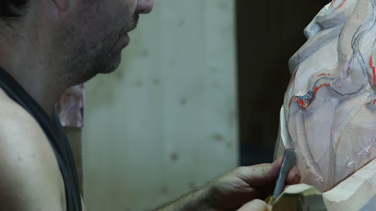 Close-up of a craftsman carving intricate details into a wooden sculpture using a chisel, showing precision, artistry, and the texture of the wood surface in a traditional workshop setting