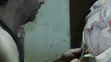 close-up of a craftsman carving intricate details into a wooden sculpture using a chisel, showing precision, artistry, and the texture of the wood surface in a traditional workshop setting