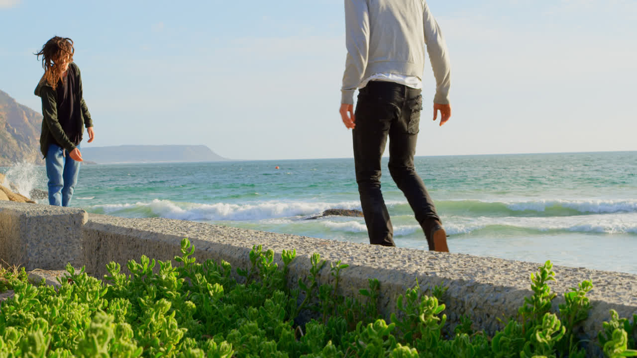 젊은 백인 남자들이 해변 4k의 보행로에서 스케이트보드 트릭을 연습하고 있습니다.