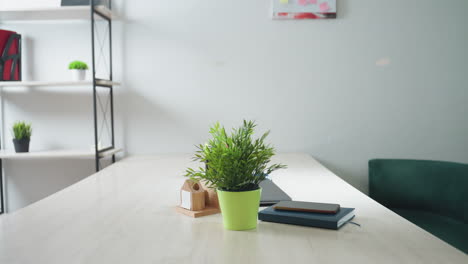 modern office interior featuring empty desk with potted plant, notebook, laptop, and phone, green couch to side, minimalist shelf with decor and creative sticky note board on white wall