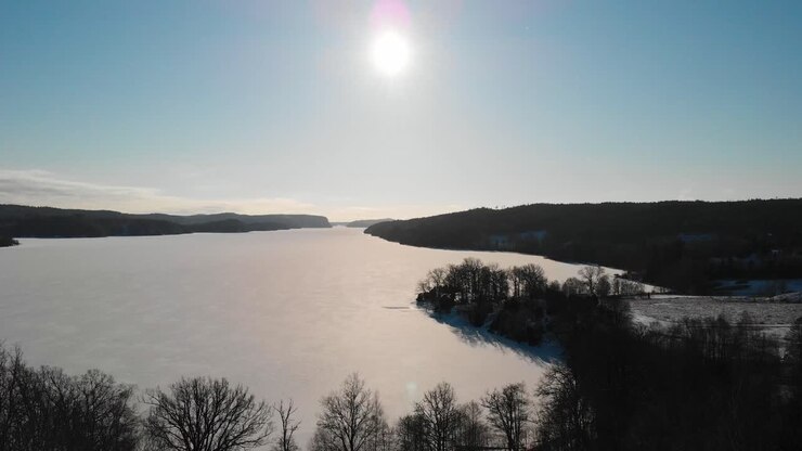 Zamrzlé jezero obklopené lesem proti jasnému slunci na modré obloze