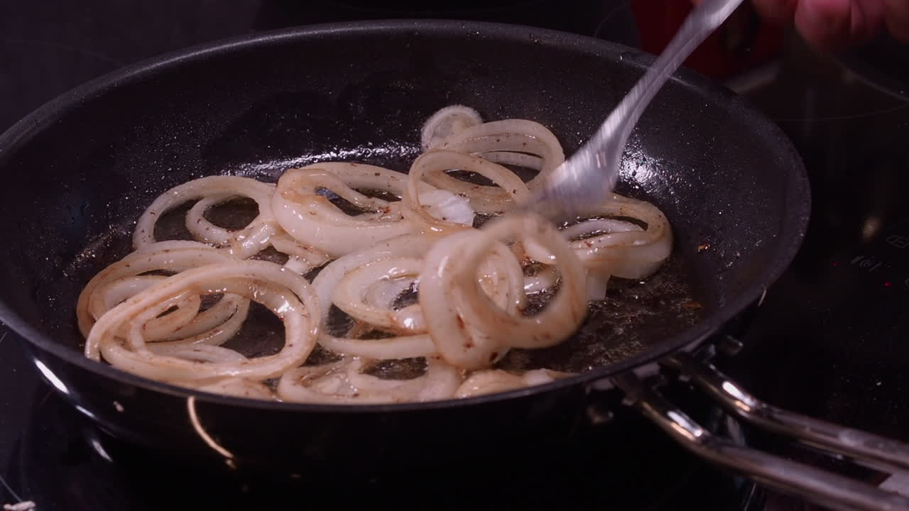 Rings of onion fry in hot frying pan, fork stirs onions sauteed in oil