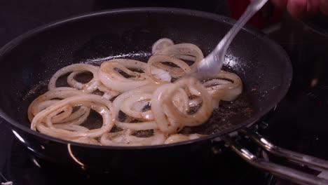 rings of onion fry in hot frying pan, fork stirs onions sauteed in oil